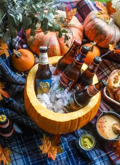 bottles of beer sit in a pumpkin shaped ice bucket on a plaid tablecloth surrounded by fall decorations