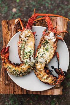 two lobsters on a white plate sitting on top of a piece of wooden plank