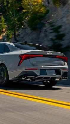 the rear end of a silver sports car driving on a road with trees in the background