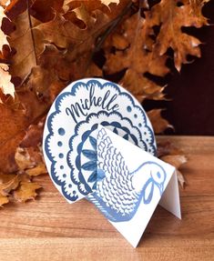 a close up of a paper turkey on a table with autumn leaves in the background