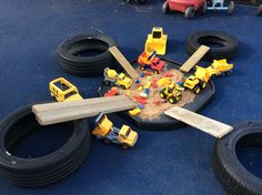 toy trucks and construction vehicles are scattered on the ground next to tires, sand and other toys