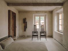 two wooden chairs sitting next to each other in a room with white walls and windows