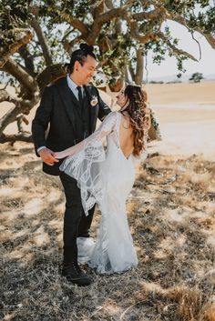 a bride and groom standing under a tree