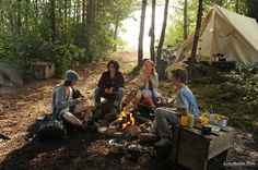 four people sitting around a campfire in the woods