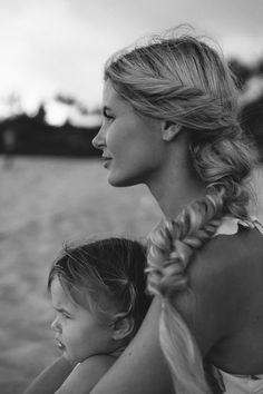 a mother and daughter sitting on the beach looking out at the water in black and white