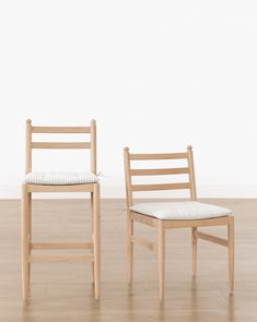 two wooden chairs sitting side by side on top of a hard wood floor next to a white wall