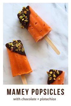 three popsicles with chocolate and pistachios are on a marble counter top