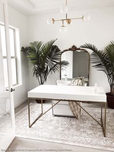 a white table and mirror in a room with potted plants on the floor next to it