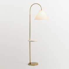 a floor lamp with a white shade on the base and a gold plated stand