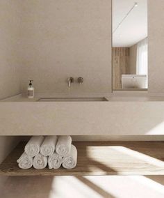 towels are stacked on a wooden shelf in front of a bathroom sink and mirror with light coming through the window