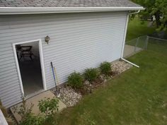 an open garage door on the side of a white house with gravel and grass around it