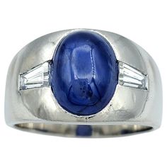 Ring size: 9.5 This striking unisex wide band ring, crafted in sleek platinum, features an extraordinary 8.50 carat oval cabochon star sapphire as its centerpiece. The mesmerizing star sapphire showcases a captivating celestial effect, drawing the eye with its natural brilliance and depth. Flanking the sapphire are two baguette-cut diamonds, adding a touch of refined elegance and enhancing the bold design. The smooth, wide platinum band offers both durability and a modern, minimalist aesthetic, Star Sapphire Ring, Wide Band Ring, Baguette Diamonds, Star Sapphire, Baguette Cut Diamond, Wide Band Rings, Timeless Jewelry, Baguette Cut, Bold Design