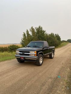 a black truck parked on the side of a dirt road