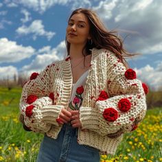 a woman standing in a field with flowers on her cardigan and looking off into the distance