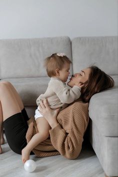 a woman holding a baby while laying on top of a couch