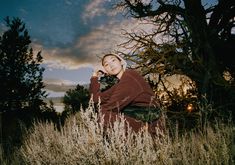 a woman is sitting in the tall grass with her hand on her chin and looking at the camera