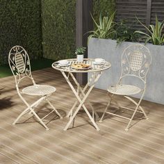 an outdoor table and two chairs on a deck with potted plants in the background