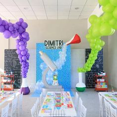 a room filled with tables and chairs covered in purple, green, and white balloons