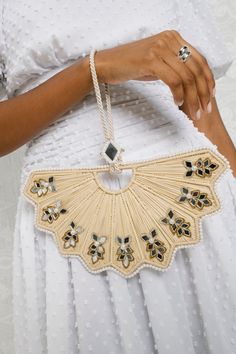 a woman wearing a white dress holding a handbag with gold and black beads on it