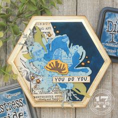 three tins with different designs on them sitting next to some leaves and flowers in front of a wooden fence