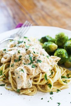 a white plate topped with pasta covered in sauce next to brussel sprouts