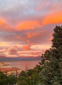 the sky is pink and orange as the sun sets over some buildings by the water