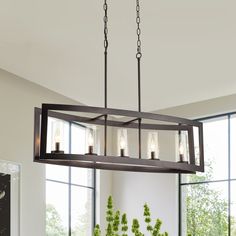 a chandelier hanging over a dining table in a room with large windows and potted plants