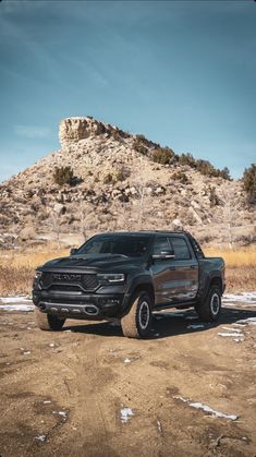 a black truck is parked in front of a mountain with no snow on the ground