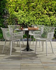 four white chairs around a table in front of a green wall with plants on it