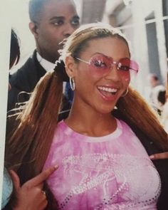 a woman with long hair and pink glasses smiling at the camera while another man looks on