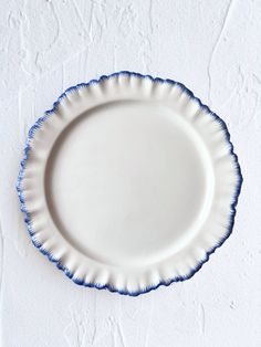 an empty white plate with blue trim on a white wall behind it is seen from above