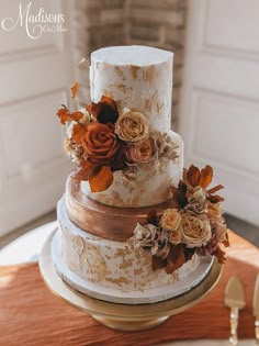 a three tiered wedding cake with flowers on the top and gold trimmings