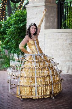 a woman in a dress made out of wine glasses is holding her hand up to the sky