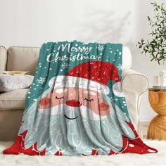 a christmas blanket with santa claus on it sitting in front of a white couch next to a potted plant