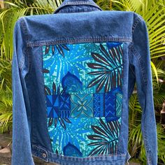 a jean jacket with blue and green designs on it, sitting in front of some palm trees