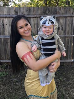 a woman holding a baby dressed as a raccoon wearing a costume on her arm