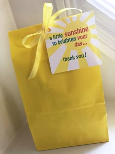 a yellow paper bag with a note attached to the handle that says, a little sunshine is to brighten your day thank you