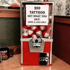 a red and white machine sitting on top of a wooden table next to a cup