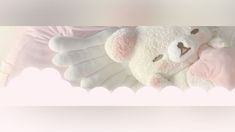 a white teddy bear laying on top of a pink blanket with wings around it's neck