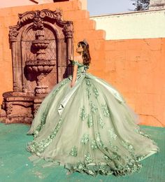 a woman in a green dress standing next to a fountain wearing a tiara with flowers on it