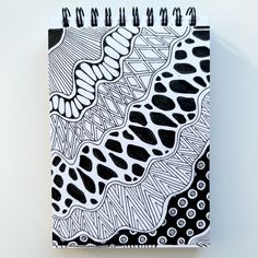 a black and white spiral notebook with an intricate design on the cover, sitting on a wall