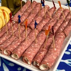 several skewered sausages and pickles are arranged on a white platter