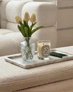 a vase with flowers on a tray next to a candle