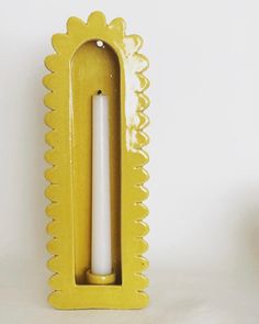 a yellow candle holder with a white candle in it