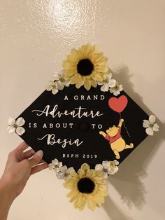 a graduation cap decorated with sunflowers and an air balloon is being held by a hand