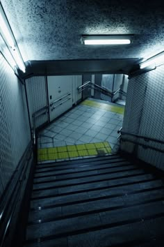 an empty stairwell with tiled floors and yellow handrails at the end is lit by two lights