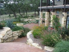 an outdoor garden with stone walls and flowers in the foreground, surrounded by trees