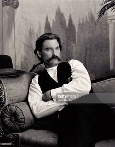 a black and white photo of a man sitting on a chair with his arms crossed