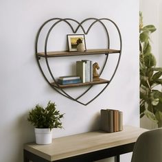 a heart shaped metal shelf with books on it next to a desk and chair in front of a white wall