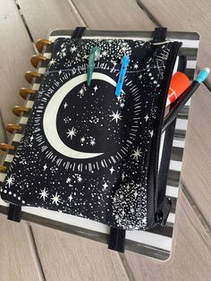 a black and white notebook with a crescent design on the cover, surrounded by stars